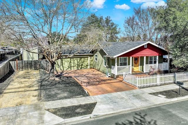 view of front of property featuring a fenced front yard, a porch, driveway, and a shingled roof