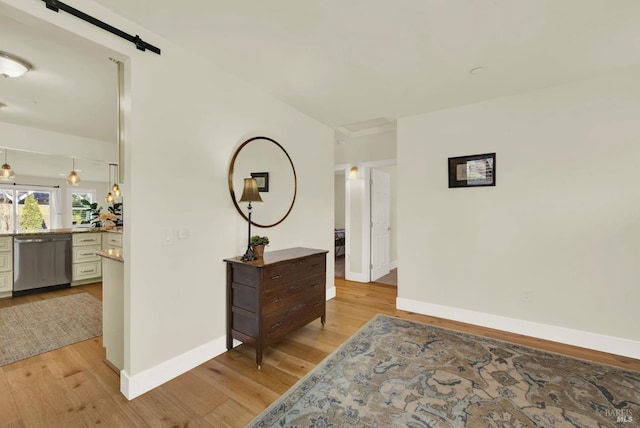 hallway with light wood-type flooring, a barn door, and baseboards