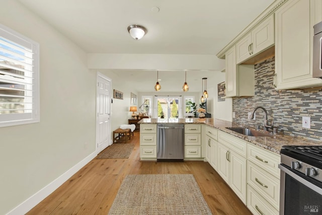 kitchen featuring a peninsula, a sink, light wood-style floors, appliances with stainless steel finishes, and tasteful backsplash