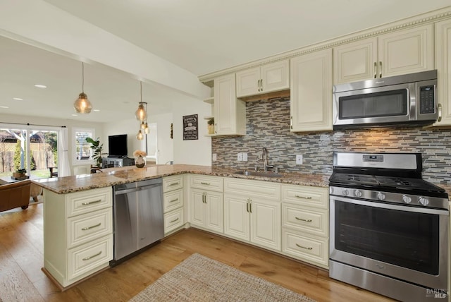 kitchen featuring a sink, stainless steel appliances, cream cabinetry, and a peninsula