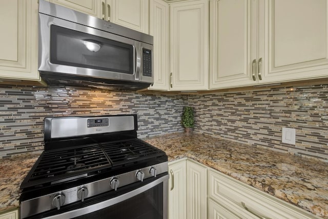 kitchen featuring light stone counters, stainless steel appliances, tasteful backsplash, and cream cabinetry