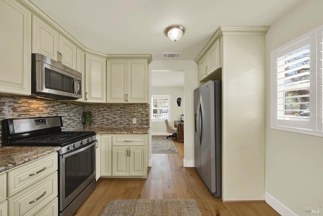 kitchen featuring visible vents, light wood finished floors, stainless steel appliances, cream cabinets, and tasteful backsplash