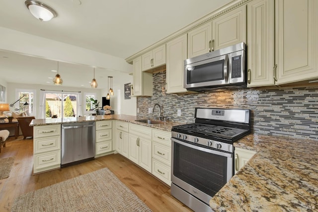 kitchen featuring light wood-type flooring, cream cabinetry, a sink, appliances with stainless steel finishes, and a peninsula