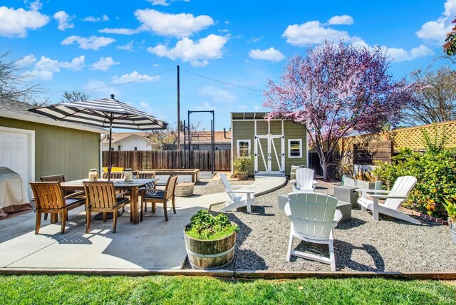 view of patio featuring an outdoor fire pit, outdoor dining area, a fenced backyard, an outdoor structure, and a storage unit