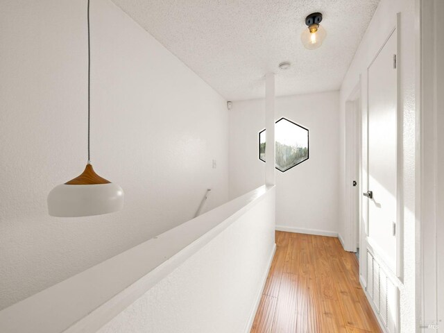 corridor with baseboards, an upstairs landing, a textured ceiling, and light wood finished floors