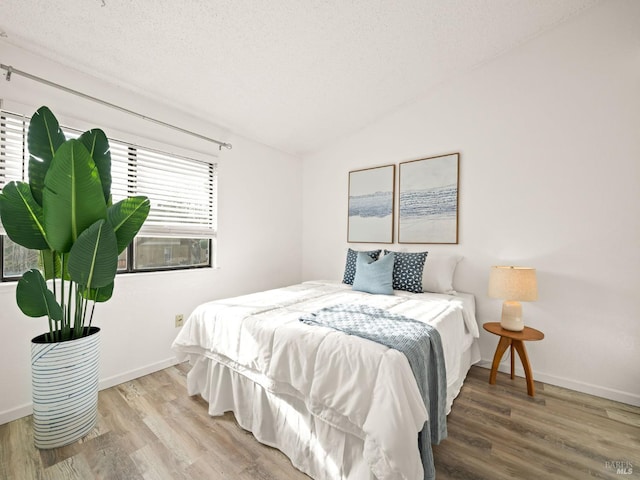 bedroom with baseboards, vaulted ceiling, wood finished floors, and a textured ceiling