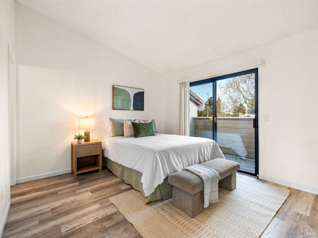 bedroom with vaulted ceiling, a textured ceiling, access to outside, baseboards, and light wood-style floors