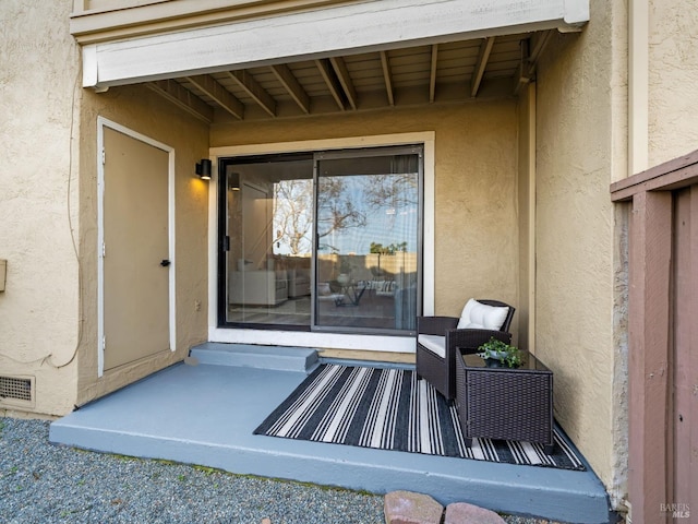 entrance to property featuring stucco siding and visible vents