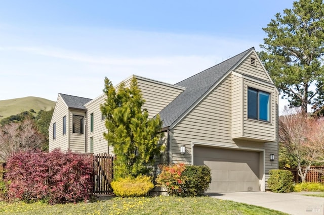 view of front of home with a shingled roof, a mountain view, concrete driveway, and fence