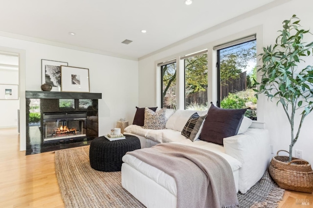 living room featuring recessed lighting, visible vents, a fireplace with flush hearth, and light wood-style flooring