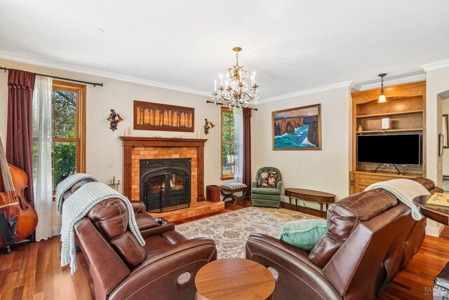 living area featuring built in shelves, a notable chandelier, wood finished floors, a fireplace, and crown molding