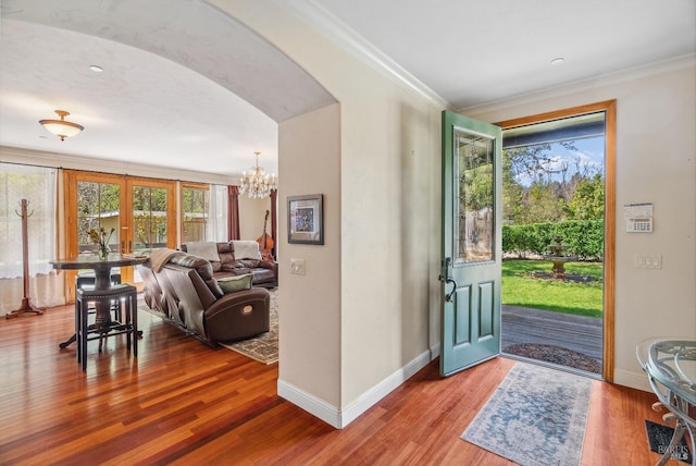 entryway featuring crown molding, wood finished floors, arched walkways, and baseboards