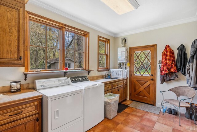 clothes washing area featuring ornamental molding, washer and clothes dryer, a sink, water heater, and cabinet space