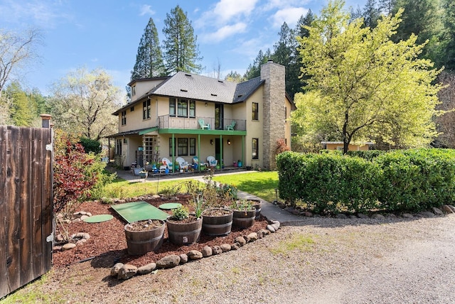 rear view of property with a patio, a balcony, fence, a chimney, and stucco siding