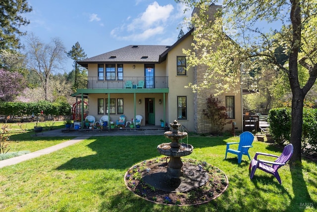 rear view of property featuring a patio, a balcony, a chimney, stucco siding, and a lawn