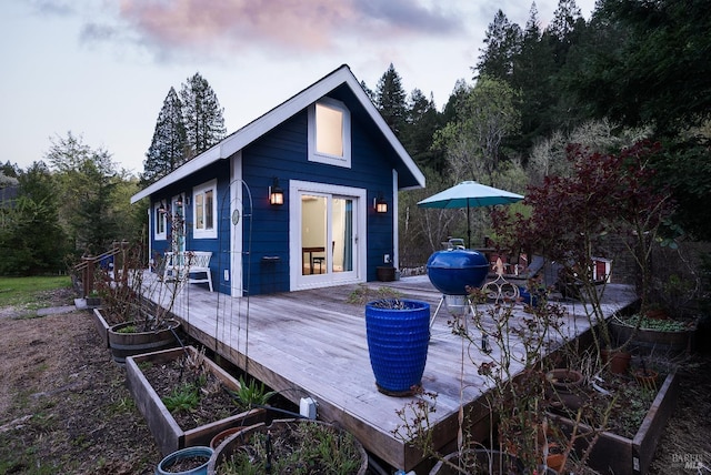 back of house at dusk with a deck, an outbuilding, and a vegetable garden