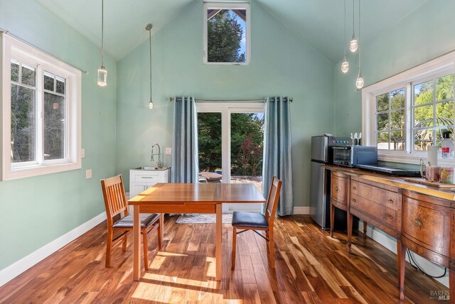 dining room with a toaster, high vaulted ceiling, baseboards, and wood finished floors