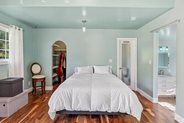 bedroom with a spacious closet, wood finished floors, arched walkways, and baseboards