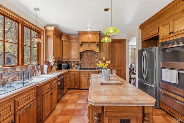 kitchen with arched walkways, a sink, tile counters, appliances with stainless steel finishes, and brown cabinets