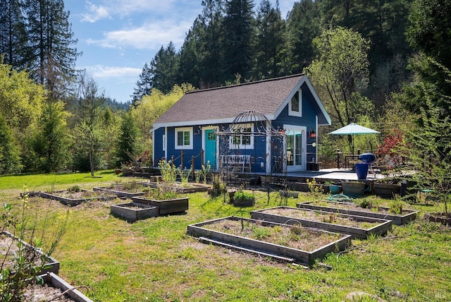 view of front facade featuring a front lawn, a garden, an outbuilding, and a view of trees