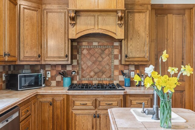 kitchen featuring brown cabinets, custom range hood, tasteful backsplash, tile countertops, and stainless steel appliances