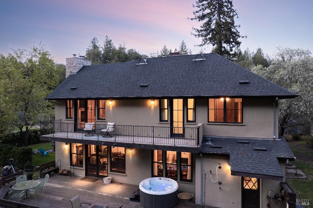 rear view of house with stucco siding, a chimney, and a shingled roof