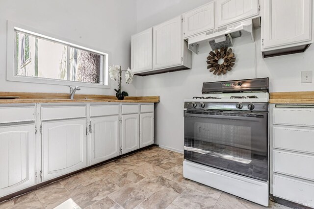 kitchen featuring a sink, white cabinetry, baseboards, under cabinet range hood, and range with gas cooktop