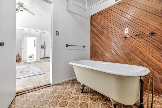 full bath with wooden walls, ceiling fan, a freestanding bath, and baseboards