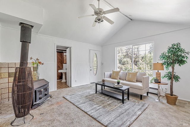 living room featuring carpet floors, a wood stove, ceiling fan, and a baseboard heating unit