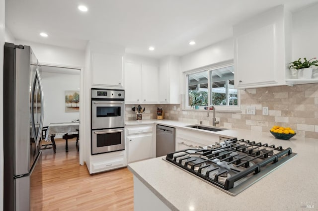 kitchen with a sink, stainless steel appliances, white cabinetry, light wood-type flooring, and backsplash