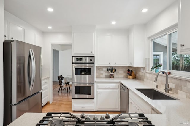 kitchen featuring a sink, decorative backsplash, light countertops, stainless steel appliances, and white cabinetry