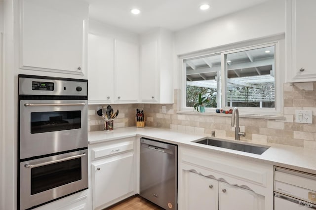 kitchen featuring a sink, backsplash, stainless steel appliances, white cabinets, and light countertops