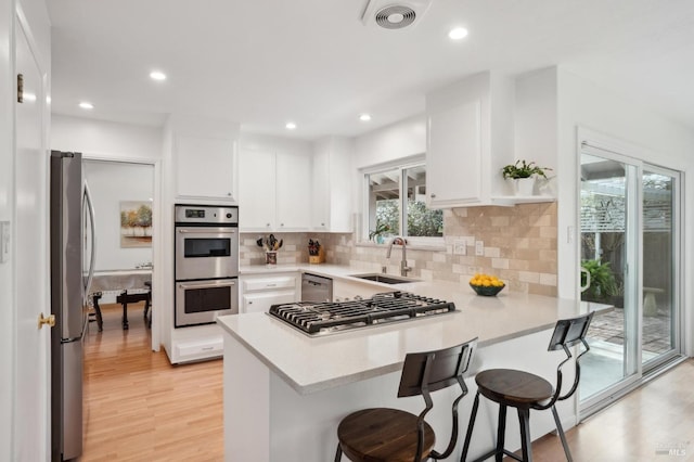 kitchen featuring visible vents, decorative backsplash, appliances with stainless steel finishes, a peninsula, and a sink