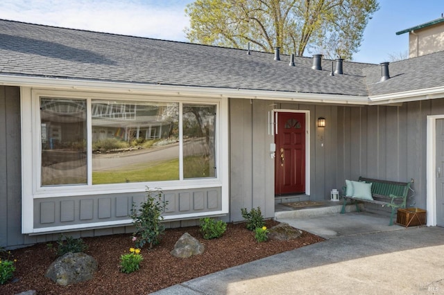 view of exterior entry featuring board and batten siding and roof with shingles