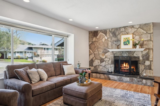 living room featuring a stone fireplace, recessed lighting, and wood finished floors