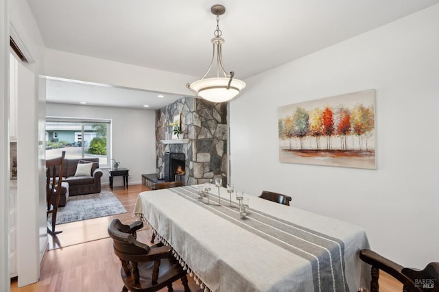 dining area with a stone fireplace, light wood-style flooring, recessed lighting, and baseboards