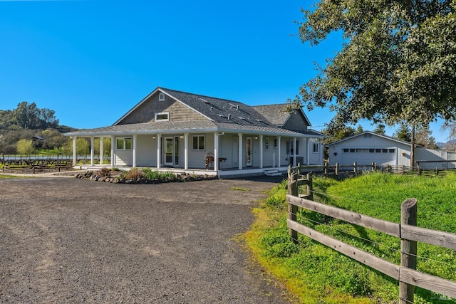 farmhouse-style home featuring a porch, fence, a garage, and an outdoor structure