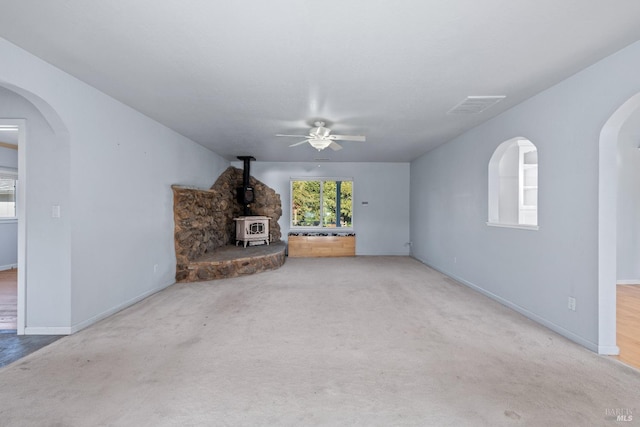 unfurnished living room featuring visible vents, a wood stove, arched walkways, ceiling fan, and carpet flooring