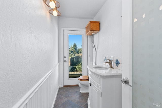 bathroom with vanity, a decorative wall, toilet, and a wainscoted wall