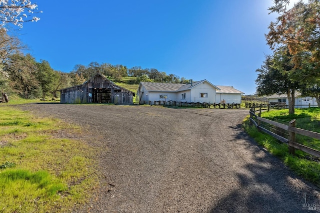 view of front of house featuring a barn, gravel driveway, an outdoor structure, and fence