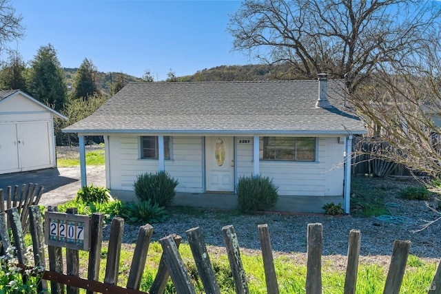 bungalow with roof with shingles, an outdoor structure, and fence