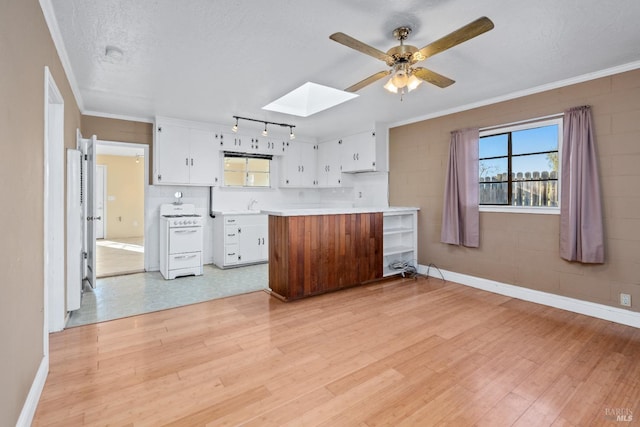 kitchen featuring light wood-type flooring, light countertops, white range with gas cooktop, a skylight, and white cabinets