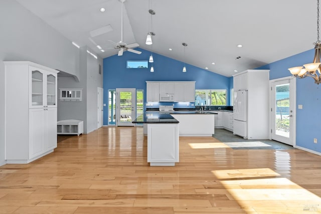 kitchen featuring white appliances, light wood finished floors, a kitchen island, white cabinetry, and dark countertops