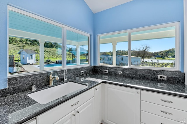 kitchen featuring white cabinetry, dark stone countertops, and a sink