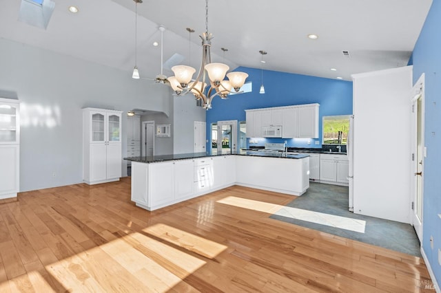 kitchen featuring light wood-type flooring, dark countertops, white cabinets, and white microwave