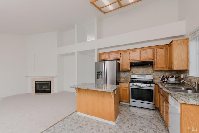 kitchen featuring a center island, under cabinet range hood, light stone counters, appliances with stainless steel finishes, and a sink