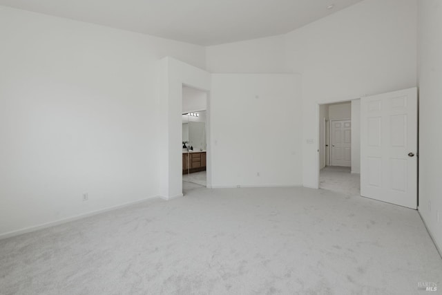 unfurnished bedroom with high vaulted ceiling, light colored carpet, baseboards, and connected bathroom