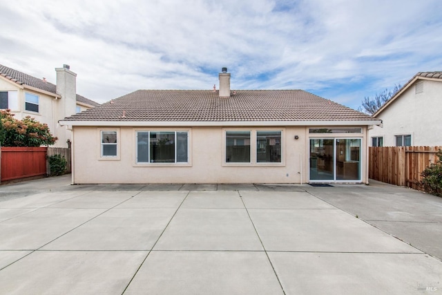 rear view of house featuring a patio area, a chimney, a tile roof, and a fenced backyard