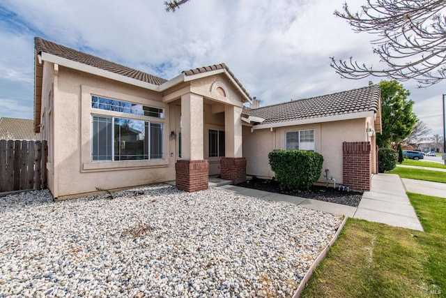 mediterranean / spanish-style home featuring stucco siding, a tiled roof, and fence