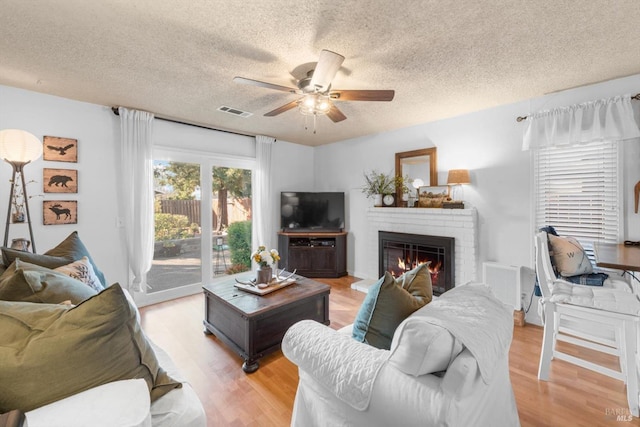 living area featuring a brick fireplace, visible vents, light wood-type flooring, and ceiling fan